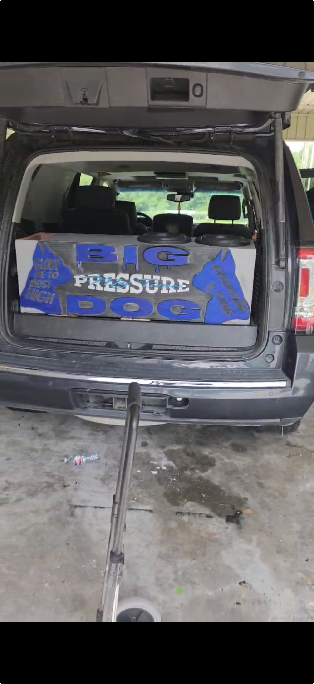 Technician installing car audio speakers and amplifier in a workshop with subwoofers and vehicle on lift