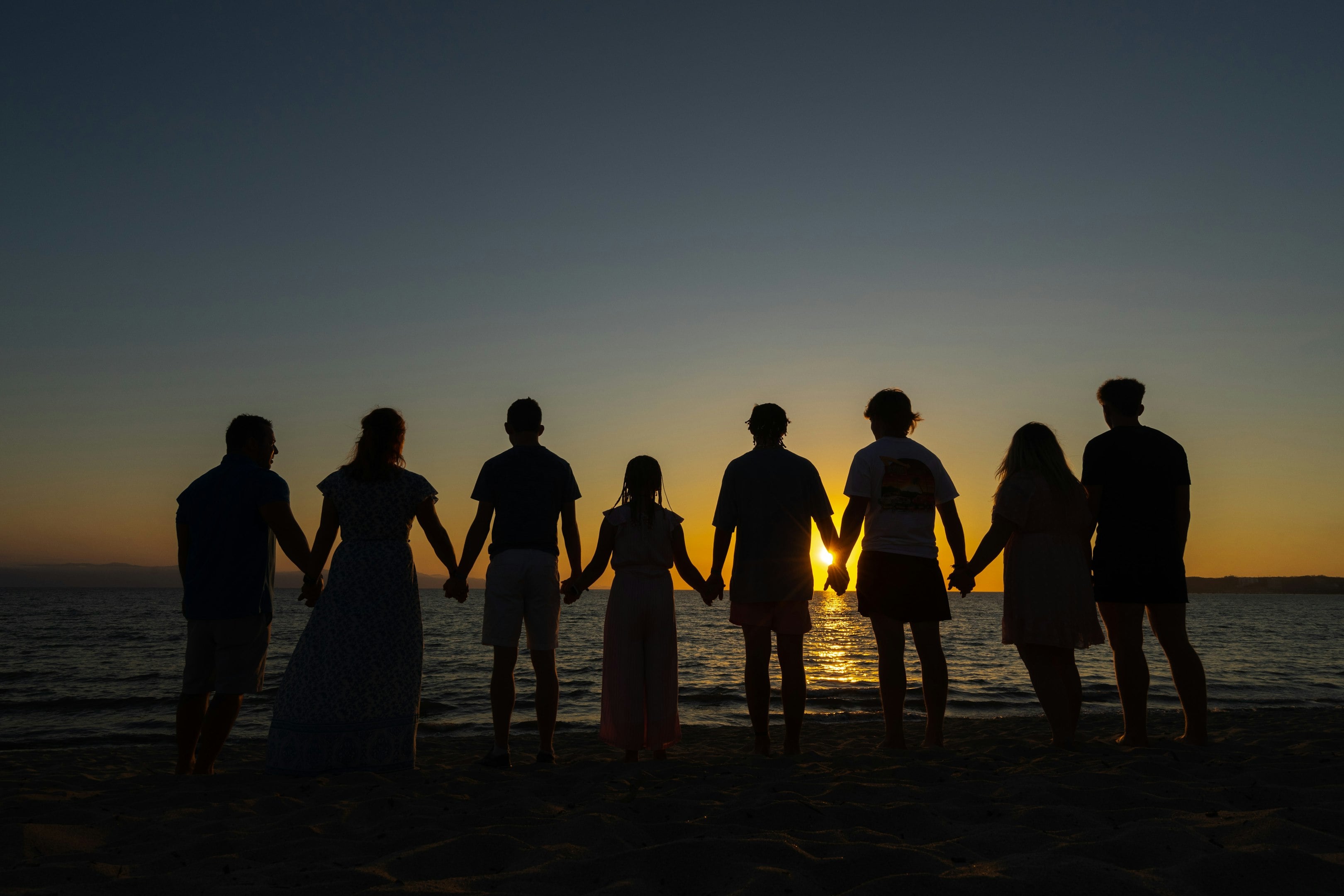 Silhouetted group of people holding hands on a beach at sunset over the ocean
