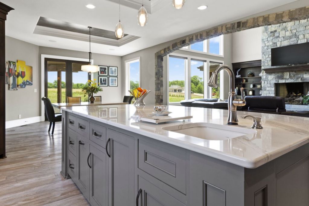 Modern kitchen interior with wooden cabinets, stainless steel appliances, a dining table with brown chairs, and large windows letting in natural light.