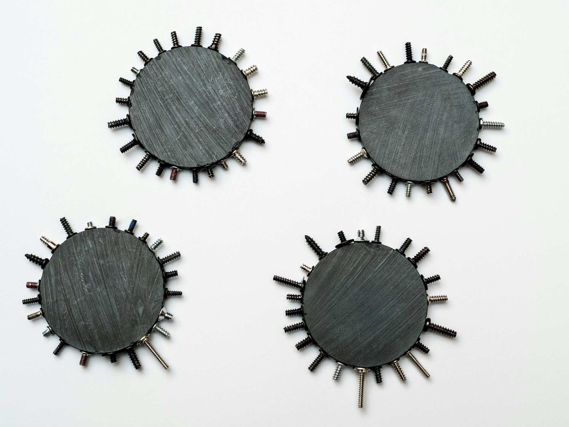 Four circular metal objects with protruding screws arranged in a symmetrical pattern on a white background.