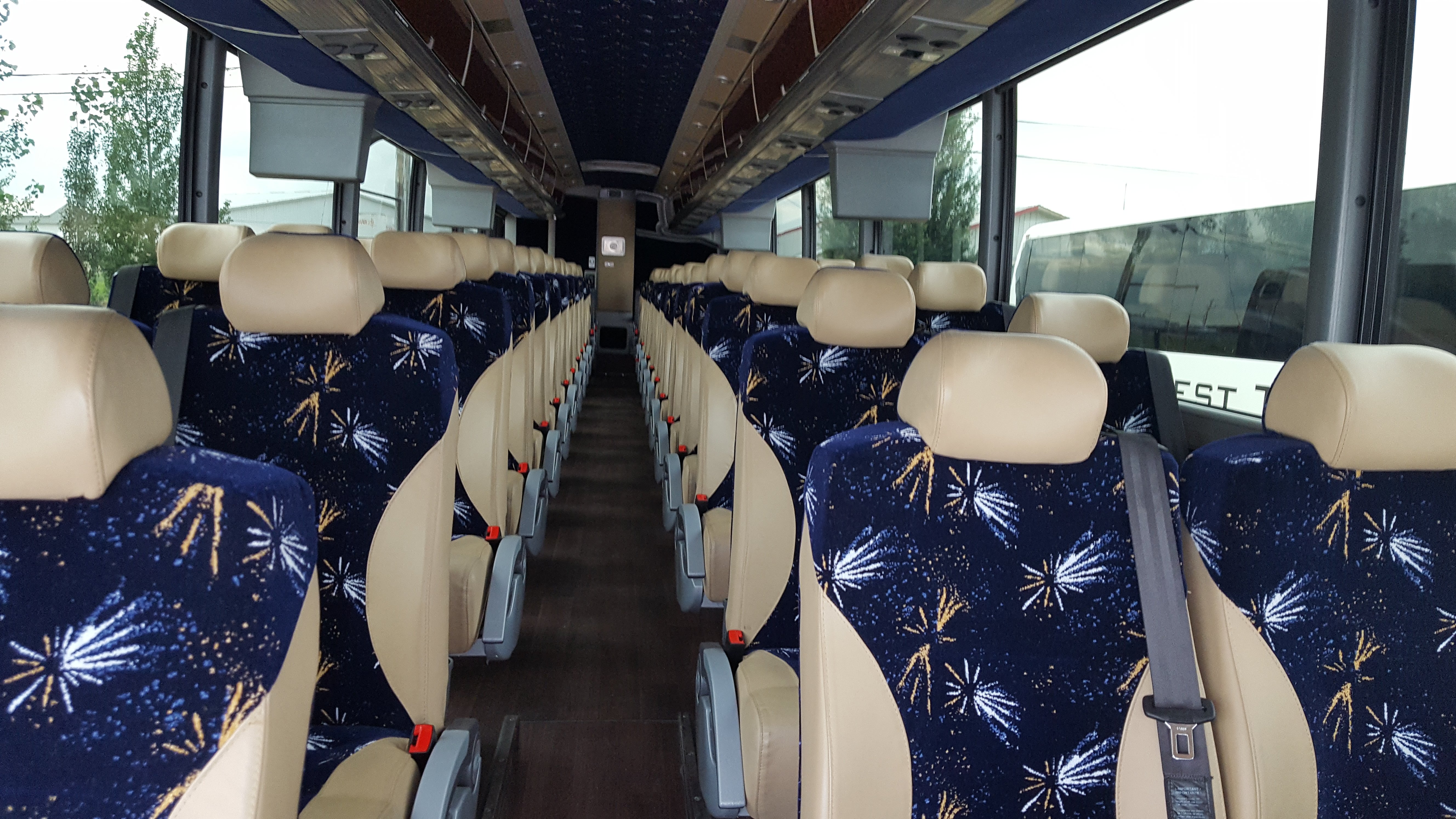 Modern white coach bus traveling on a scenic mountain road with vibrant autumn foliage and distant snowy peaks under a clear blue sky.