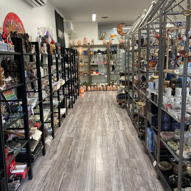 Interior of a crystal shop with shelves displaying various stones, ornaments, and spiritual items on a wooden floor.