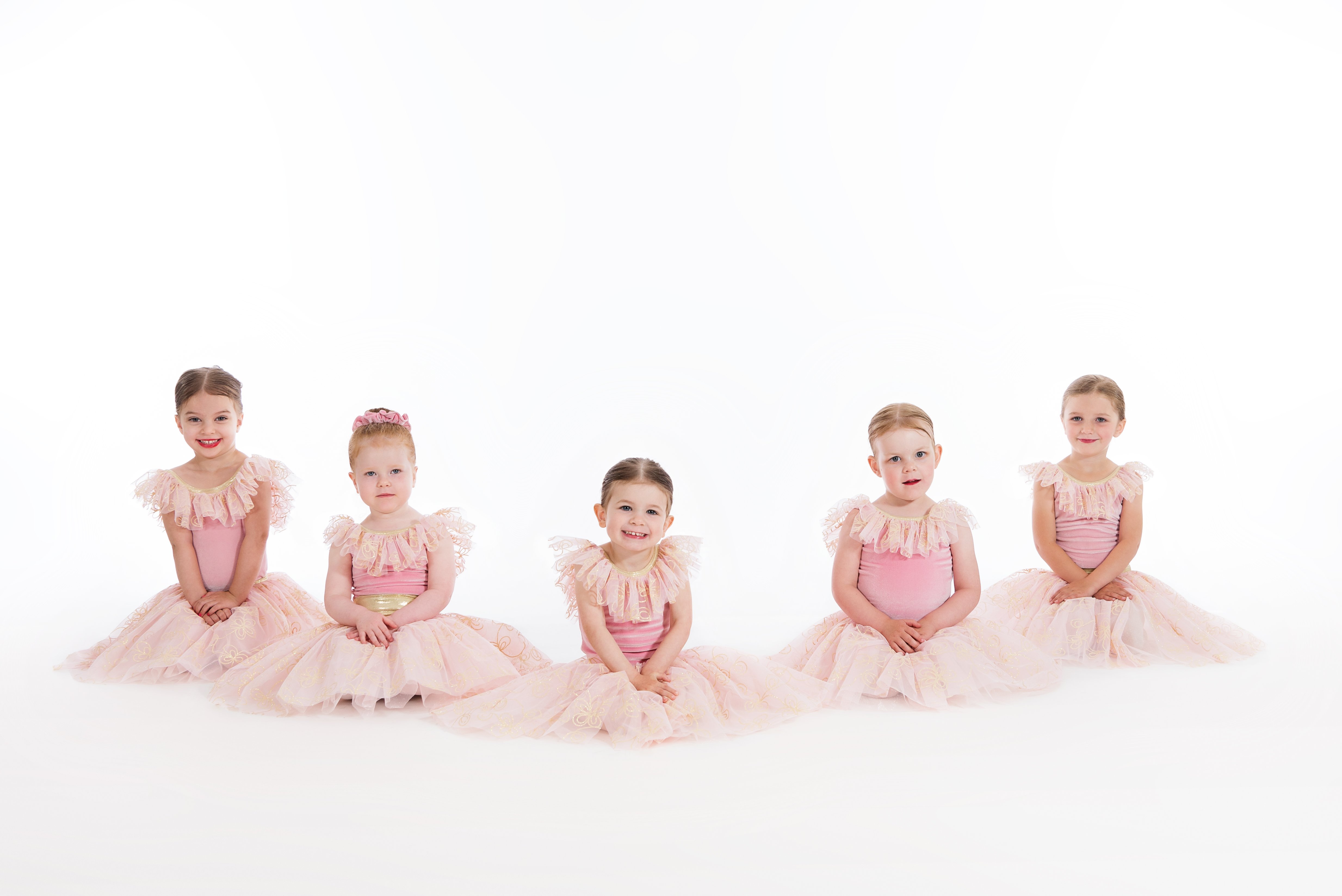 Five young girls in matching pink ballet costumes posing in a row on a white background.