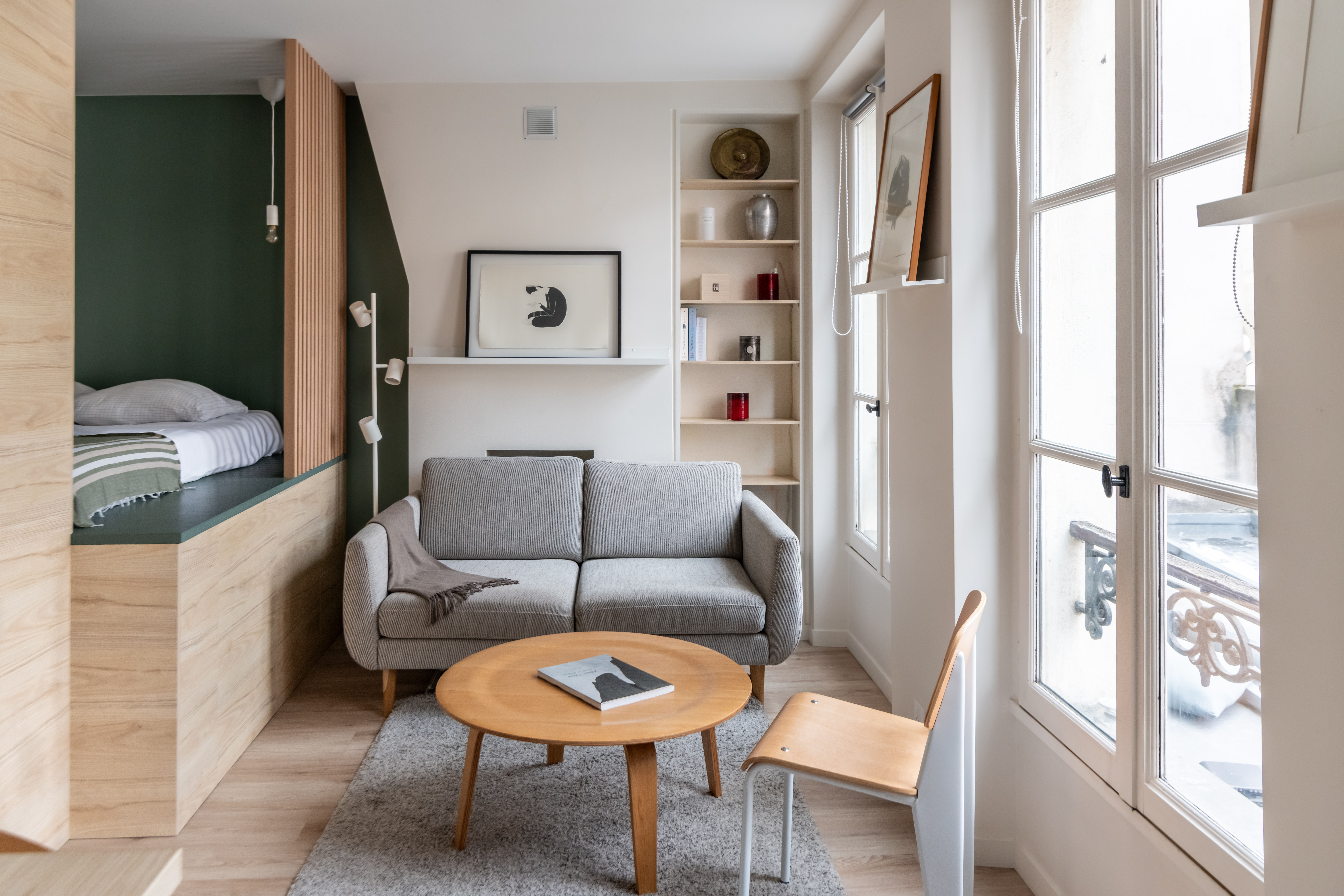 Salon moderne avec canapé bleu, table basse noire, plantes et rideaux blancs, décoration minimaliste.