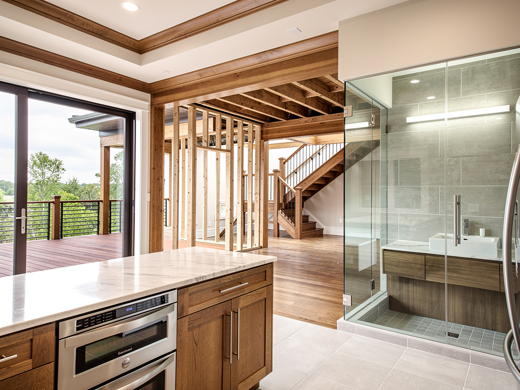 Modern open-concept home interior with wood beams, kitchen island, glass shower, staircase, and deck view