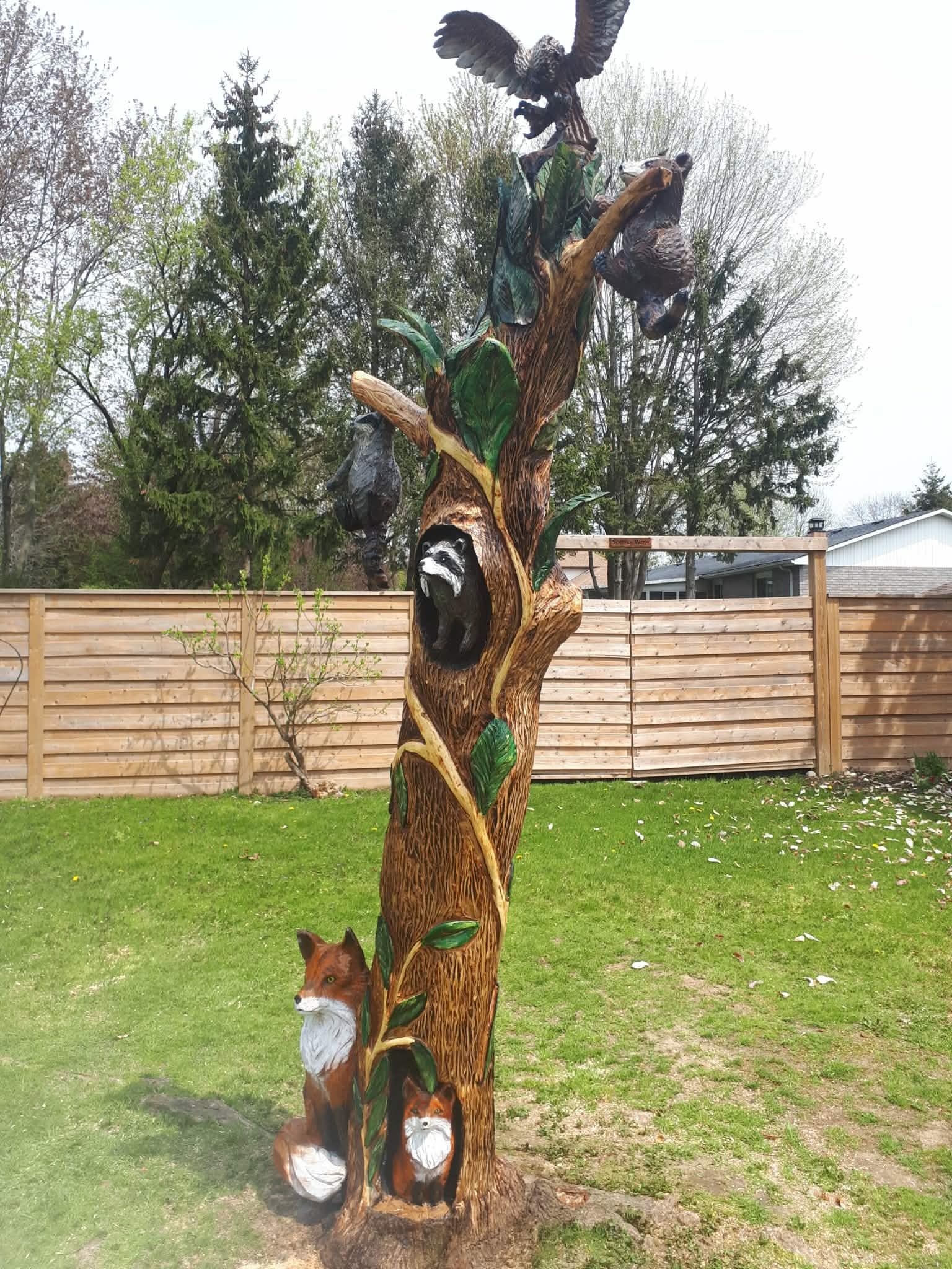 Wood carvers using chainsaws to create bear and owl sculptures in a sunny backyard