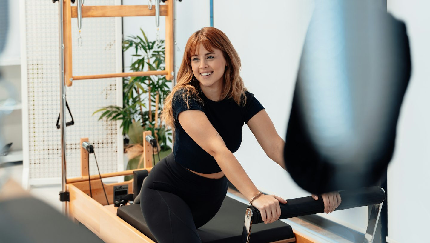 Woman practicing yoga in a modern sunlit room with plants, wearing black activewear, sitting in a meditative pose on a yoga mat.