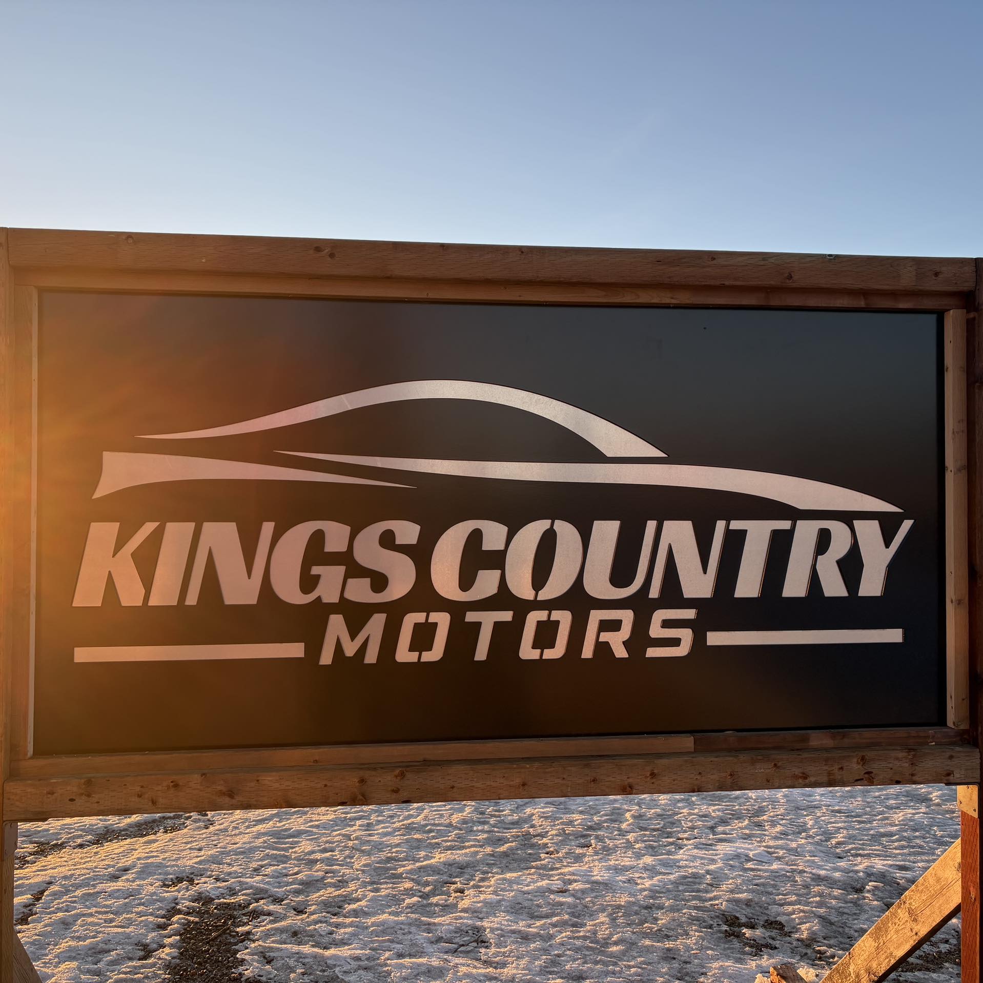Signboard of Kings Country Motors with car silhouette, illuminated by sunset light, set against a snowy background.