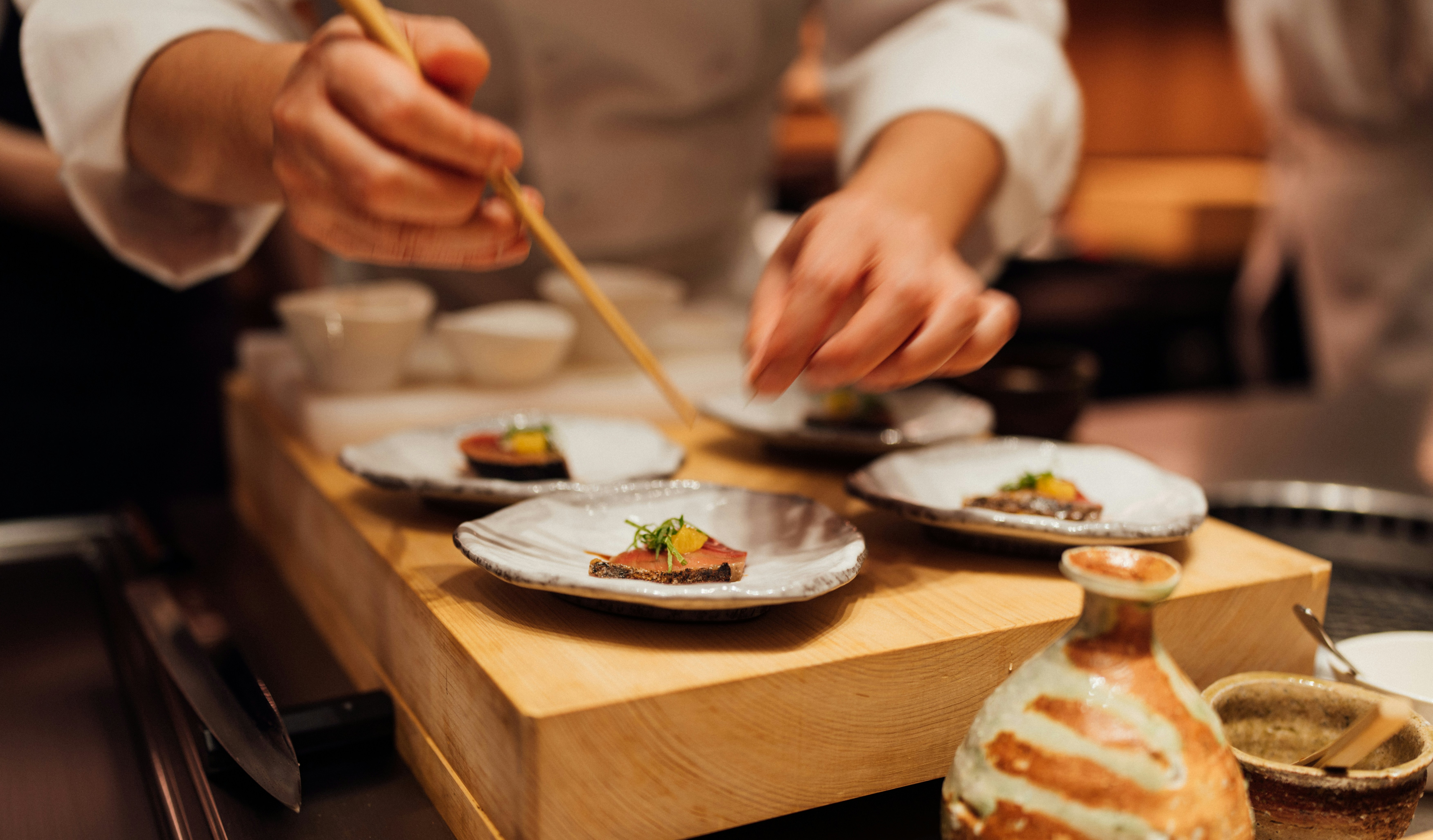 Chef meticulously plating a gourmet dish with chopsticks, showcasing intricate culinary presentation in a restaurant setting.