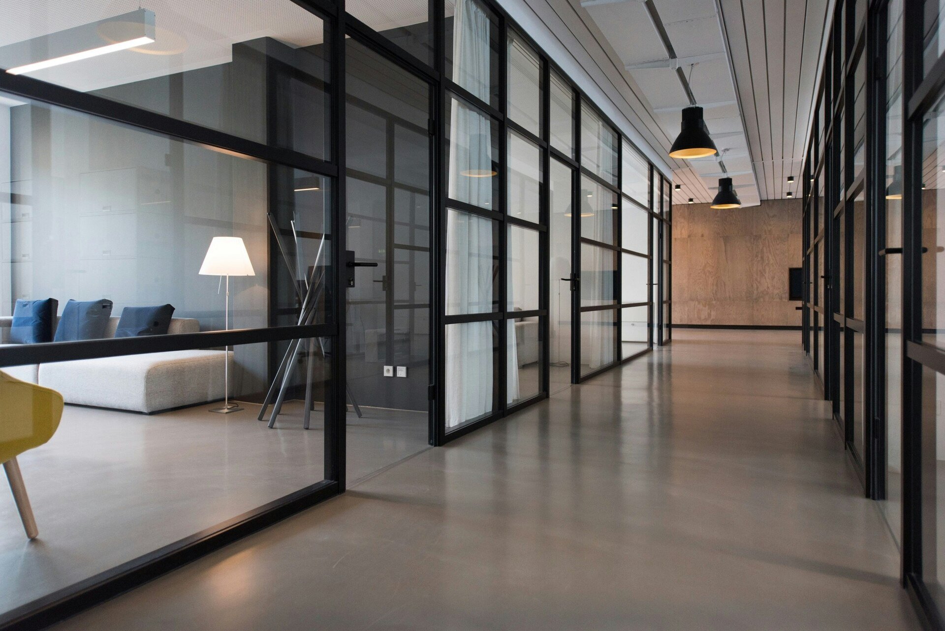 Modern office corridor with glass partitions, minimalist decor, and ambient lighting.