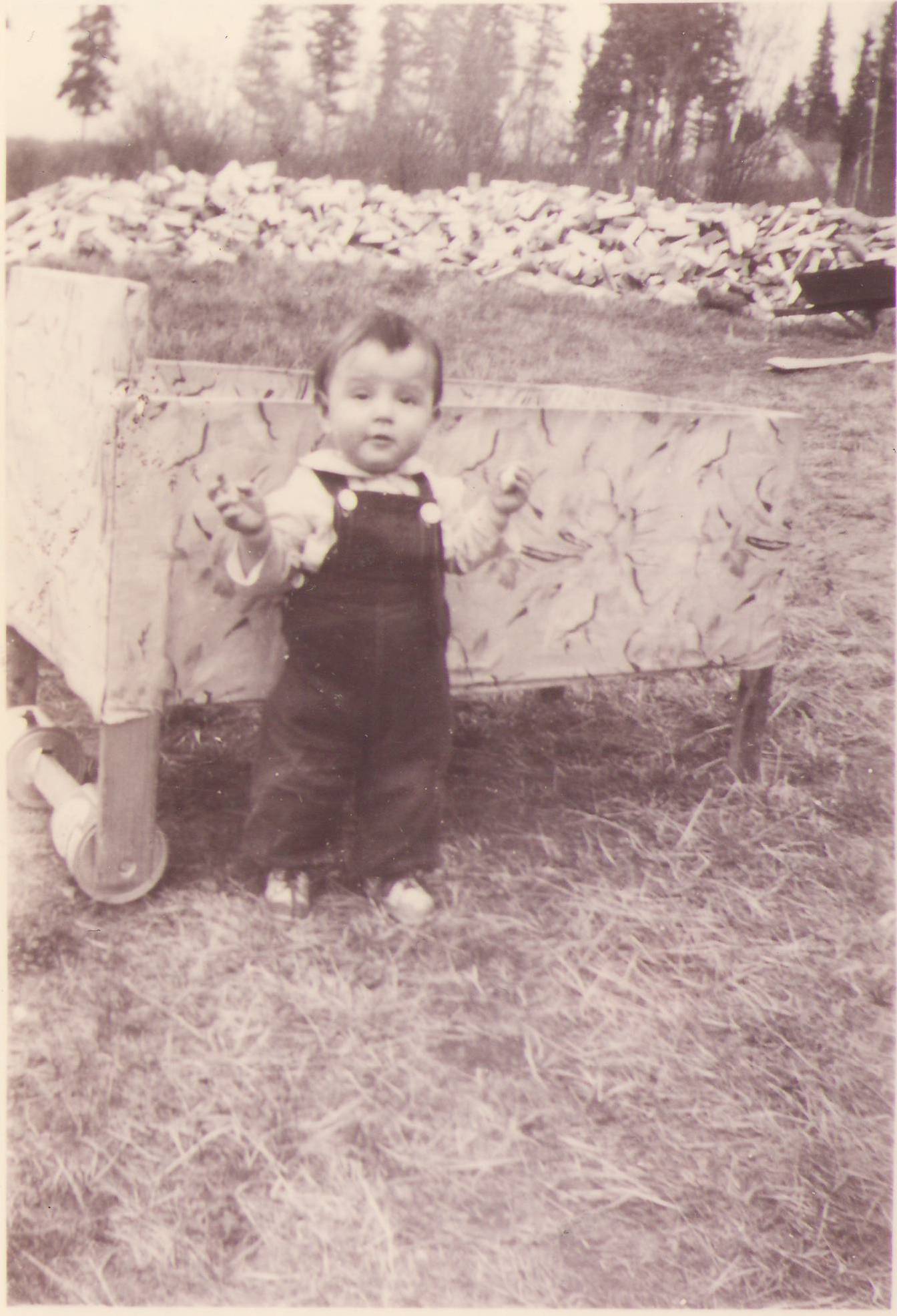 Look how cute this little one is - it appears they have a snack in one hand and attitude in the other! We are also big fans of the wheels made of tin cans on the pram in the back - very creative! Let us know if you recognize who this little one is.
990.4.106.9 / Ward, Vera