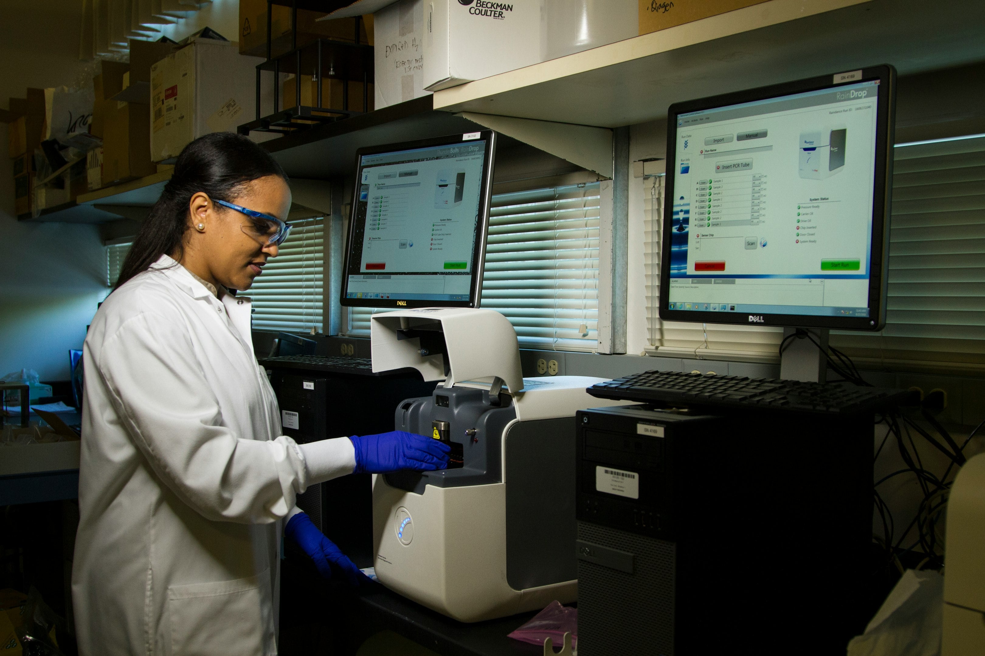 Scientist in lab coat using laboratory equipment while analyzing data on dual monitors. Scientist in lab coat using laboratory equipment while analyzing data on dual monitors.