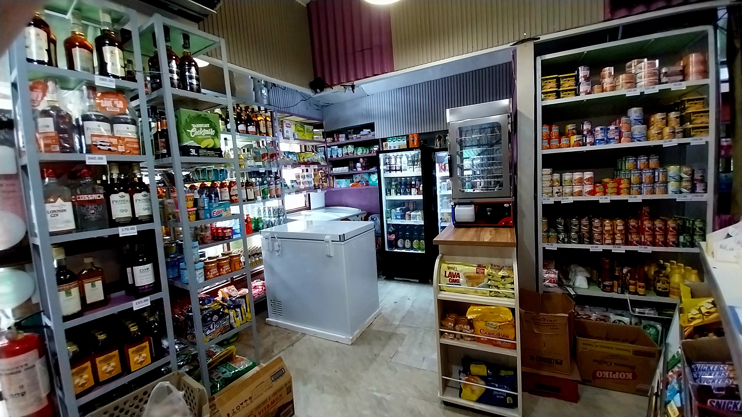 Interior of a well-stocked grocery store with shelves filled with beverages, canned goods, snacks, and various food items.