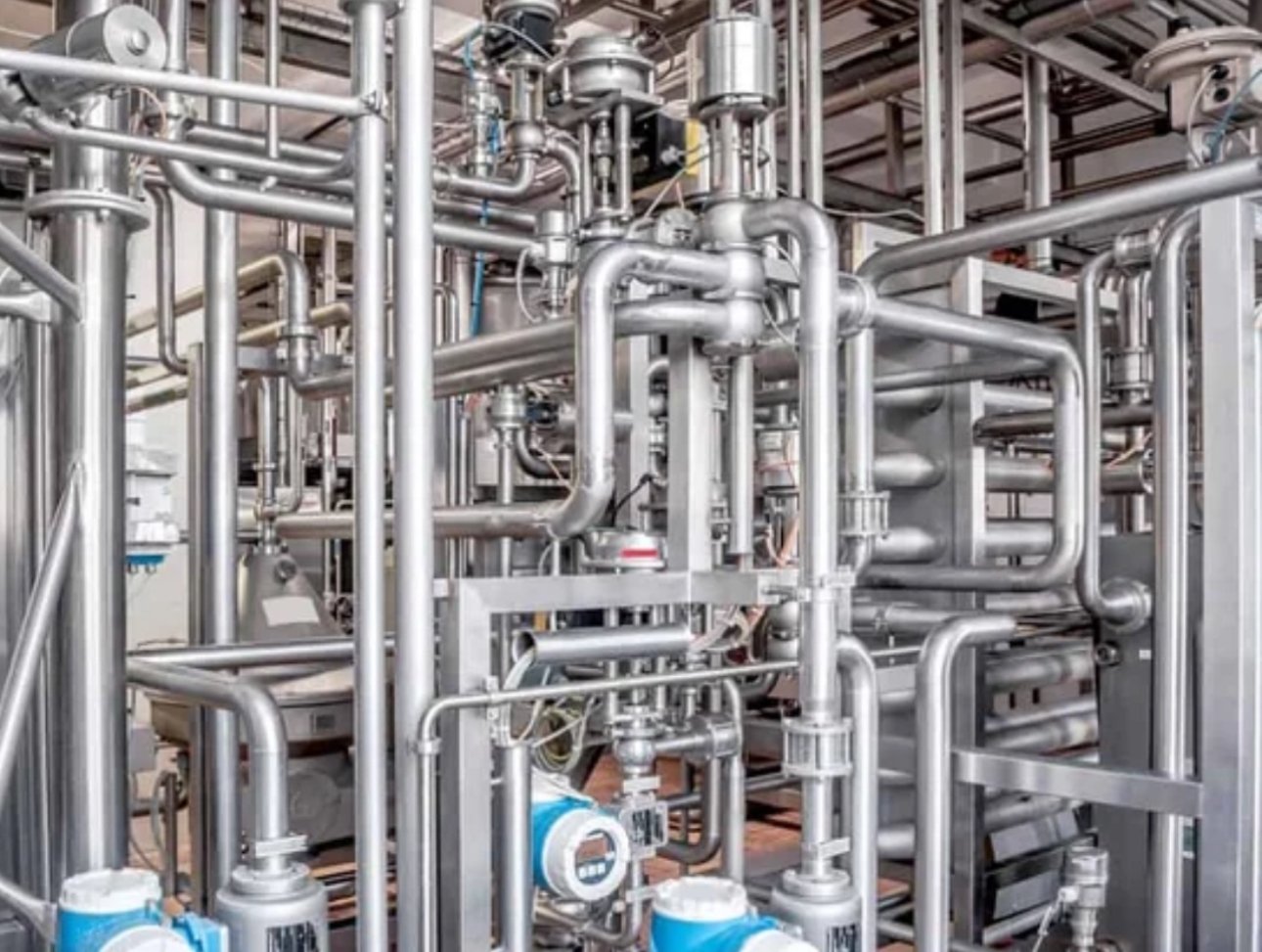 Industrial facility with large metal pipes and scaffolding, featuring a red Micro19 mec lift and complex piping infrastructure.