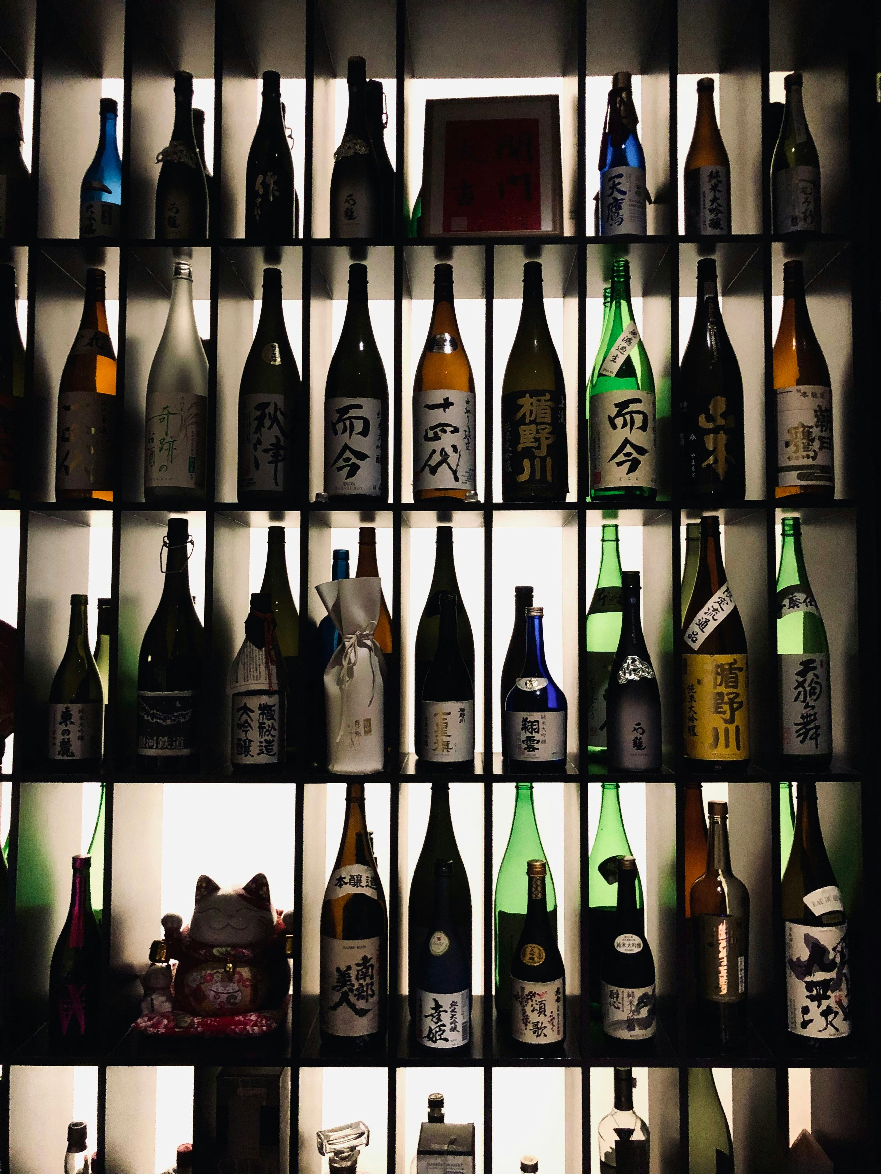 Assorted sake bottles displayed on an illuminated shelf with various labels in Japanese characters.