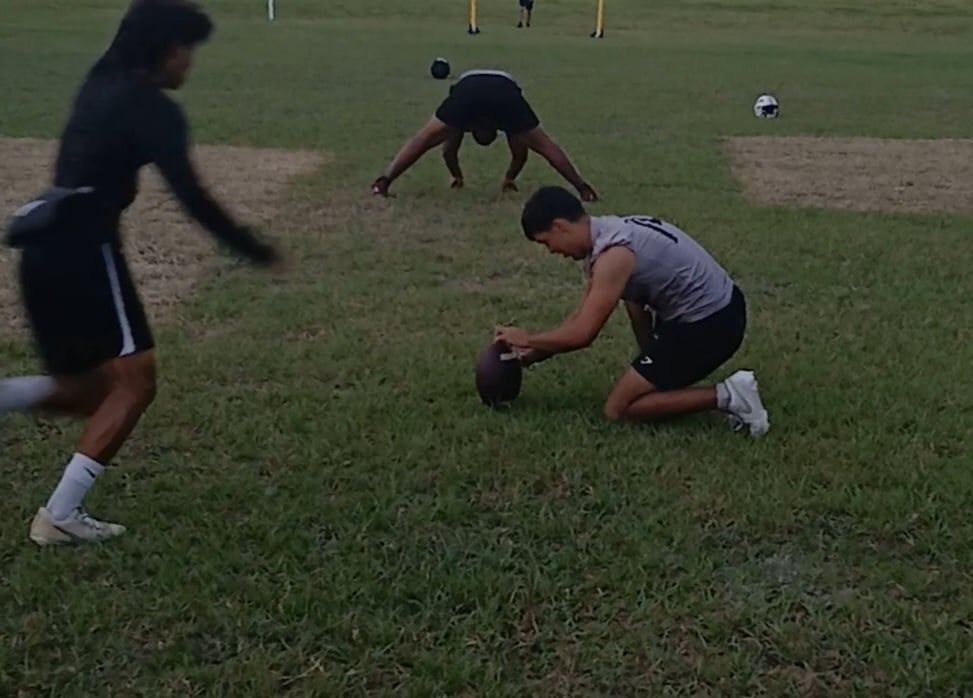 Football players practicing field goals on a grassy field with goalposts in the background.