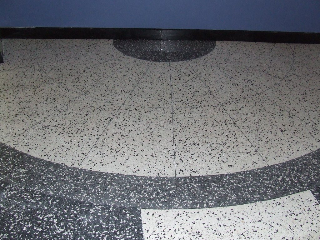 Modern open-concept kitchen and living room with granite floor, sleek appliances, large windows, and indoor plants.