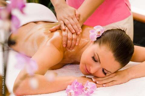 Relaxing spa massage with aromatherapy, woman lying on massage table with pink orchids and oil massage therapy.