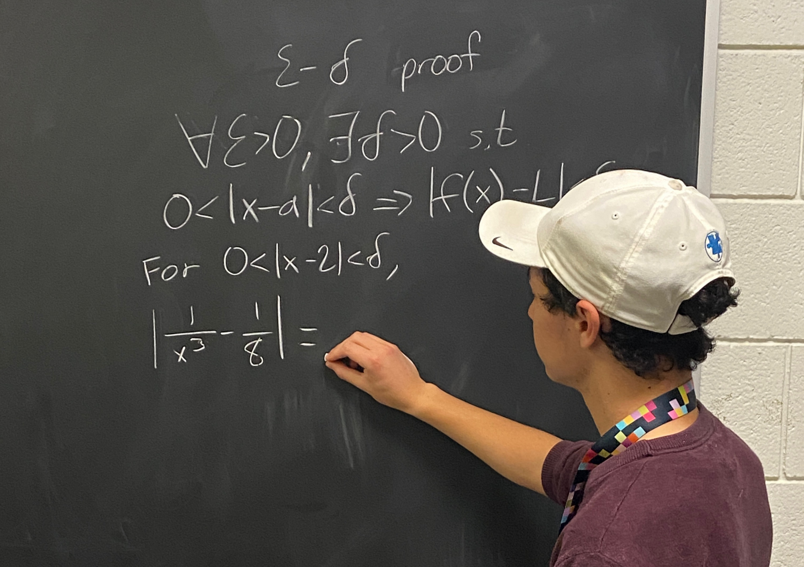 Student writing epsilon-delta proof and calculus equations on classroom chalkboard