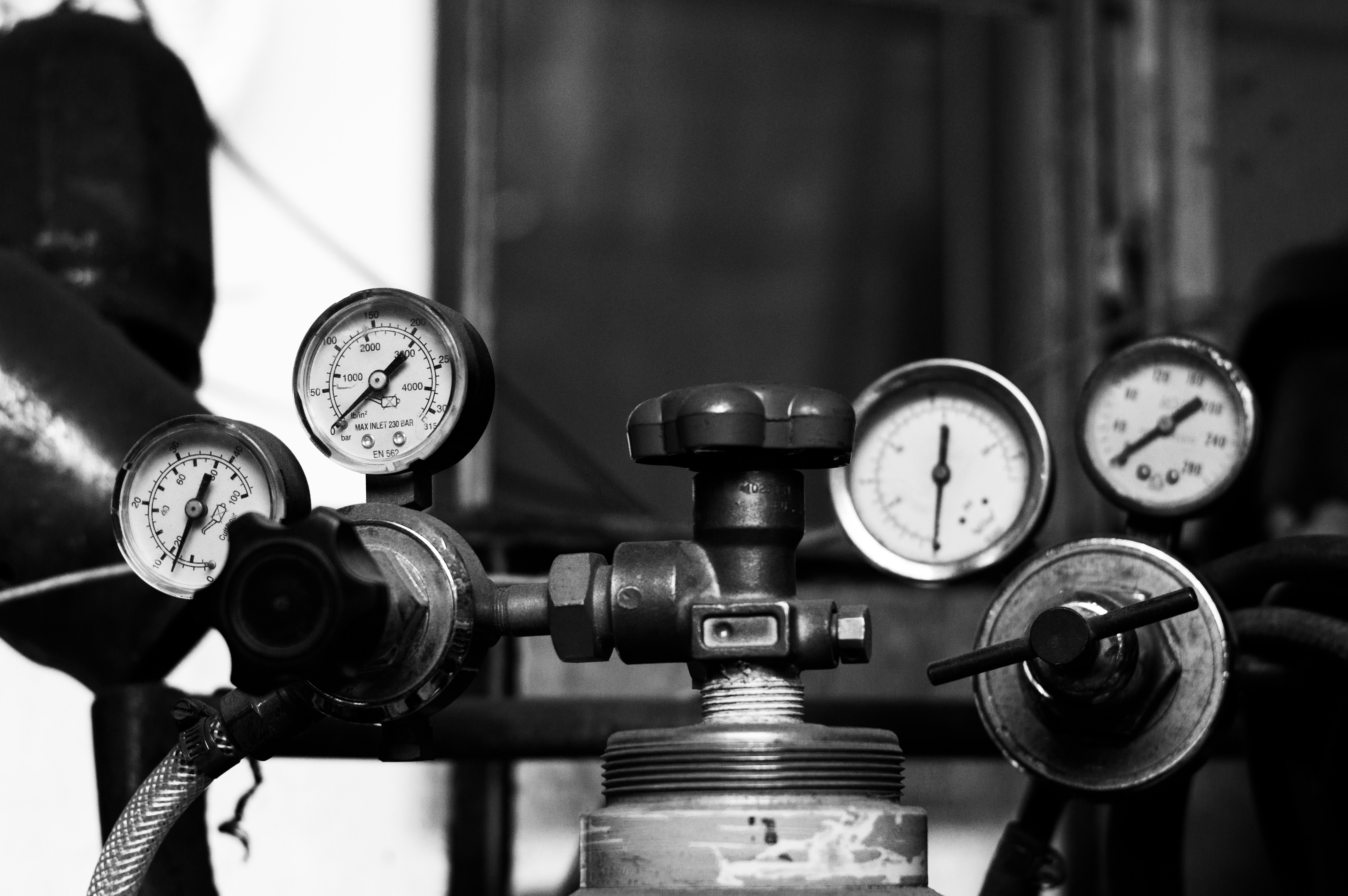Close-up of industrial pressure gauges and valves in black and white.