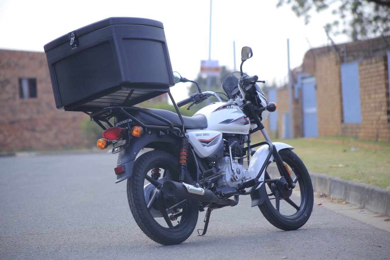 Rear view of a parked white motorcycle with a large black storage box on a street.