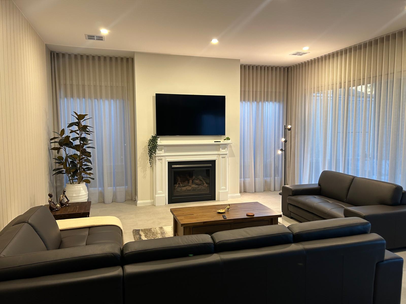 Modern living room with a beige sectional sofa, round wooden coffee table, large abstract wall art, potted plants, and floor-to-ceiling windows. Modern living room with a beige sectional sofa, round wooden coffee table, large abstract wall art, potted plants, and floor-to-ceiling windows.