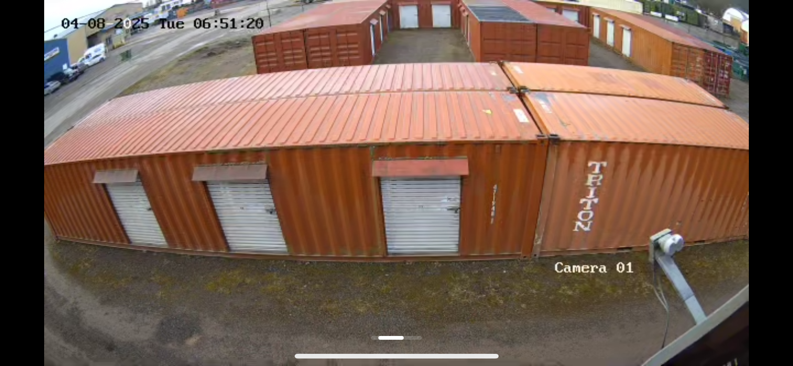 Overhead view of orange shipping containers with security camera monitoring area, timestamped April 8, 2025.