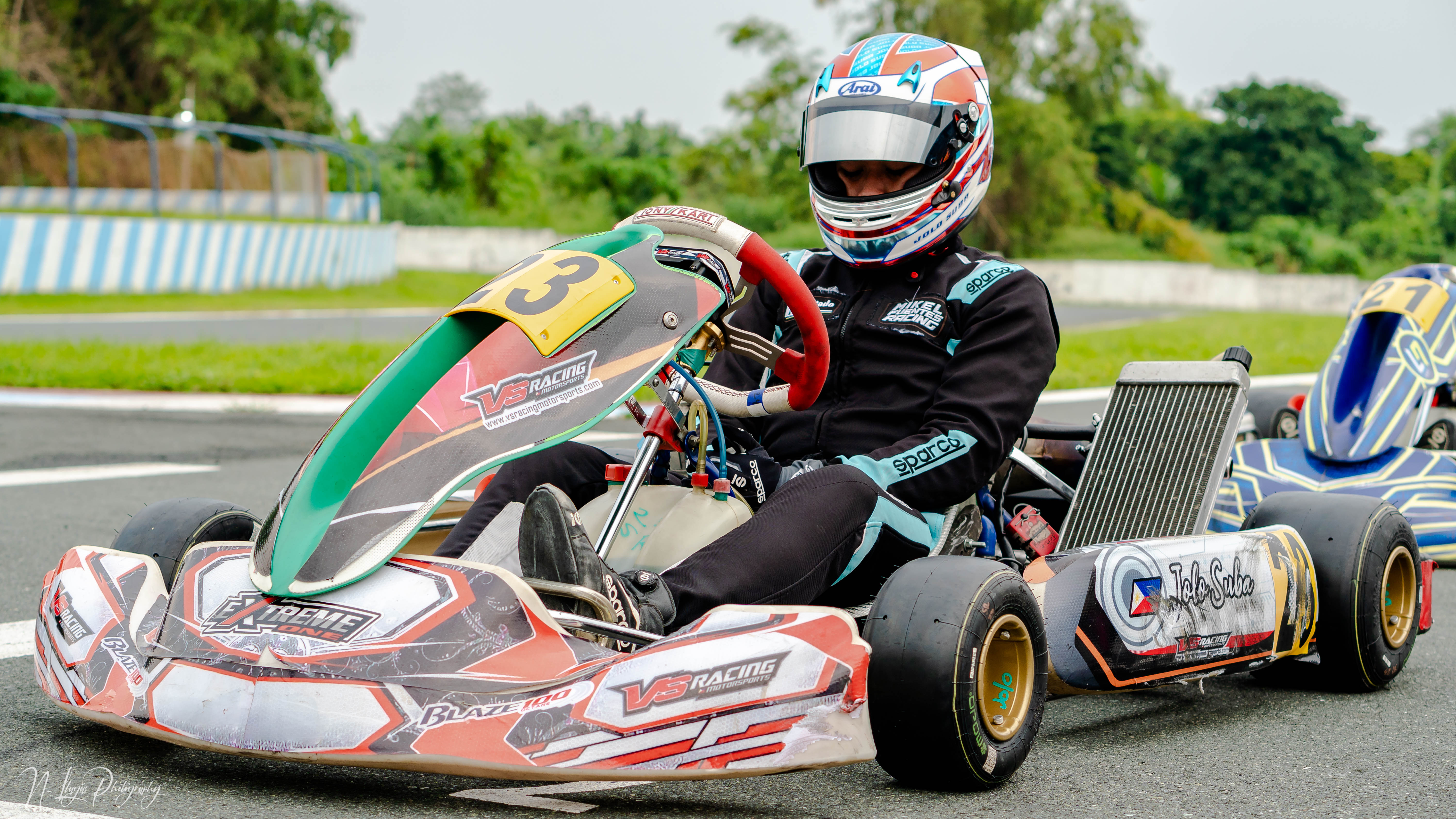 Person in a racing suit driving a red go-kart with the number 32 on a track. Person in a racing suit driving a red go-kart with the number 32 on a track.