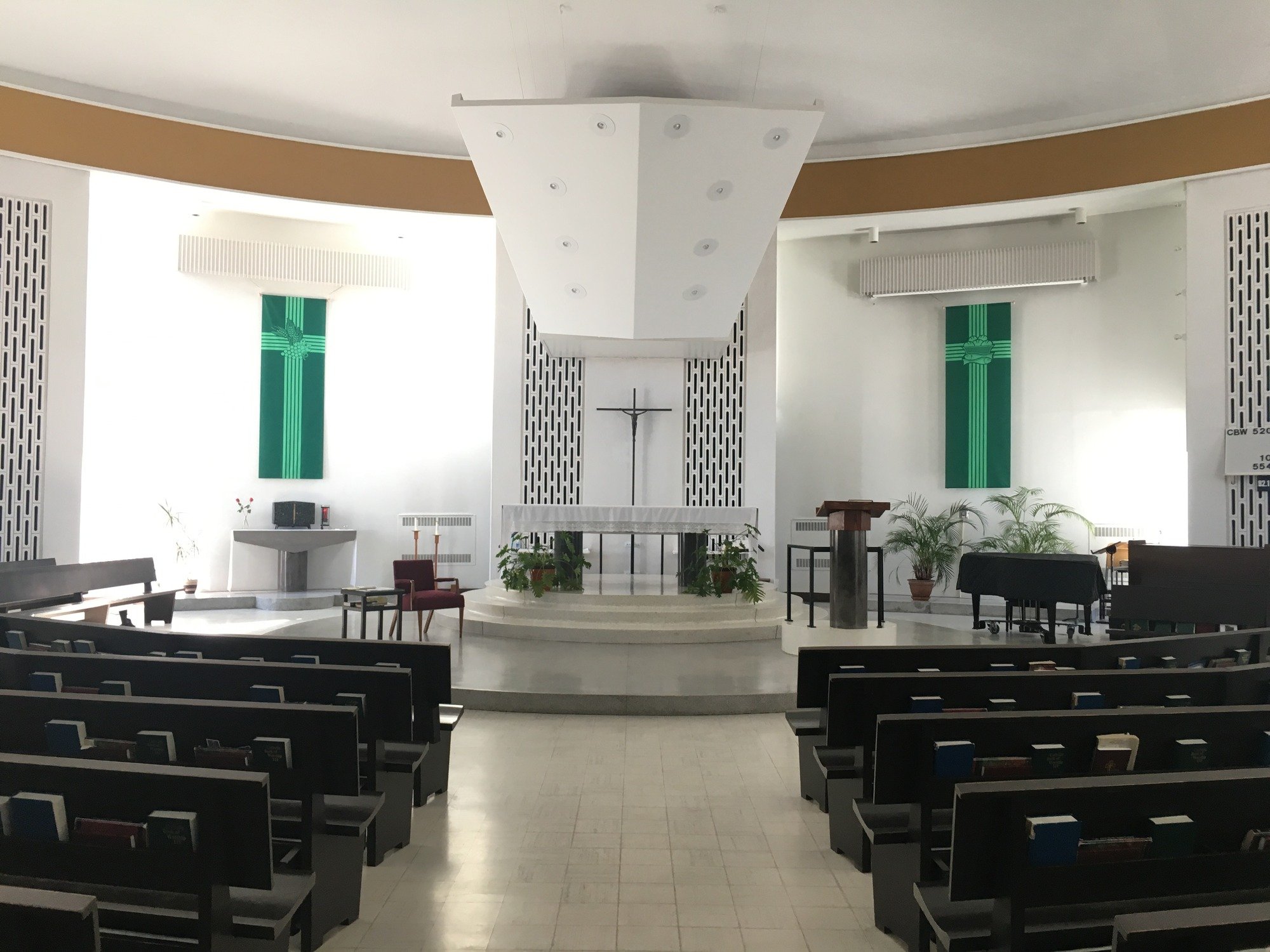Modern church interior with a wooden cross on the wall, inspirational text, indoor plants, and brown chairs arranged on a stone platform. Modern church interior with a wooden cross on the wall, inspirational text, indoor plants, and brown chairs arranged on a stone platform.