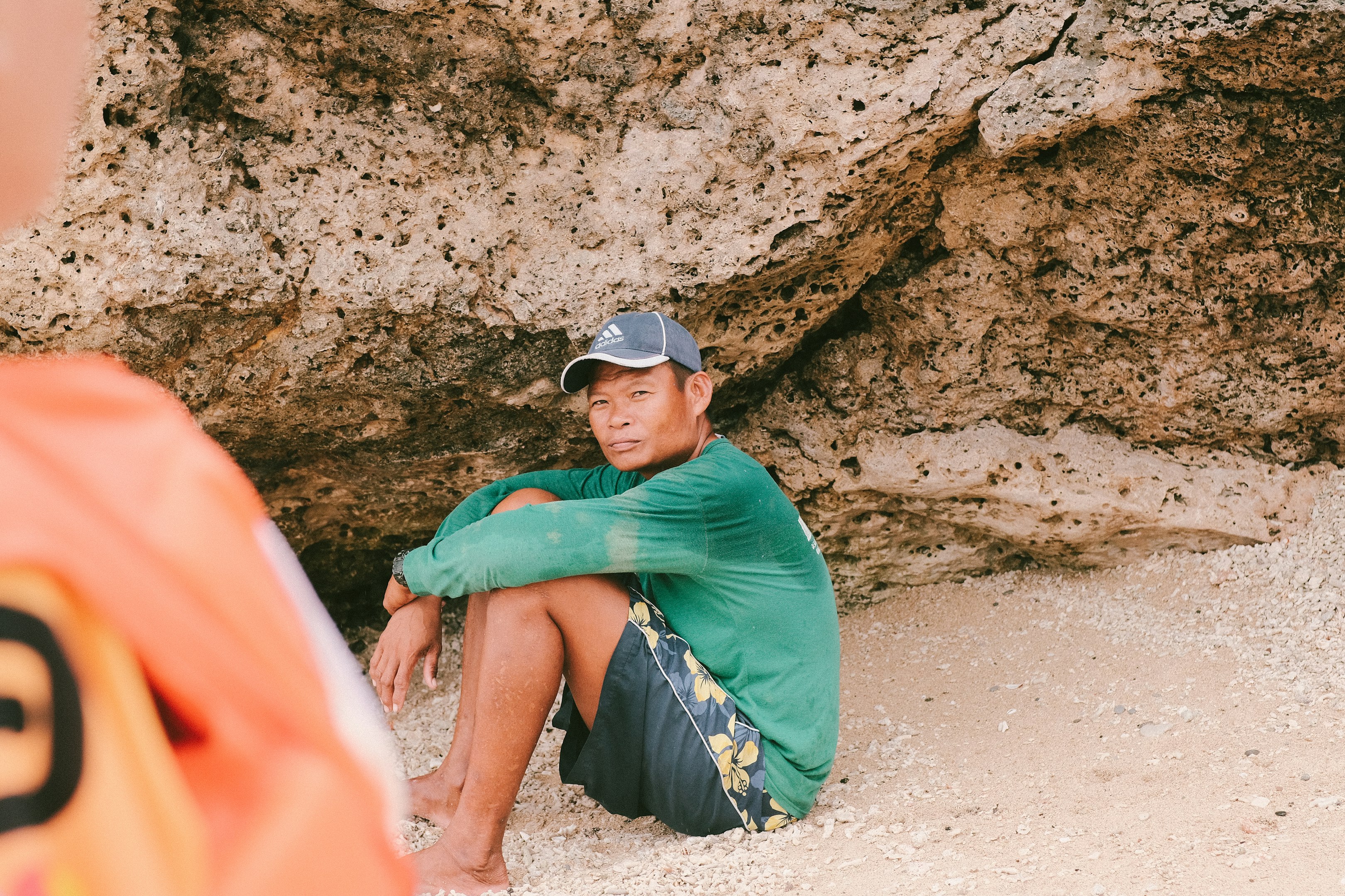 a man sitting on the ground next to a rock