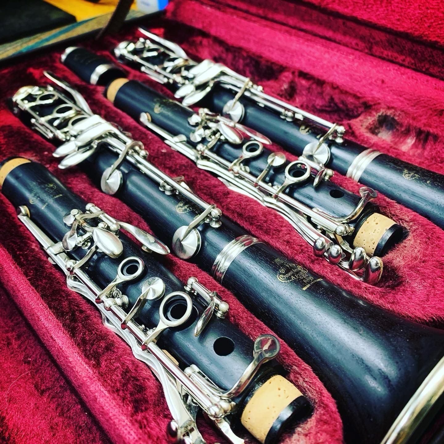 Vintage clarinet surrounded by various brass instrument parts on a dark surface.