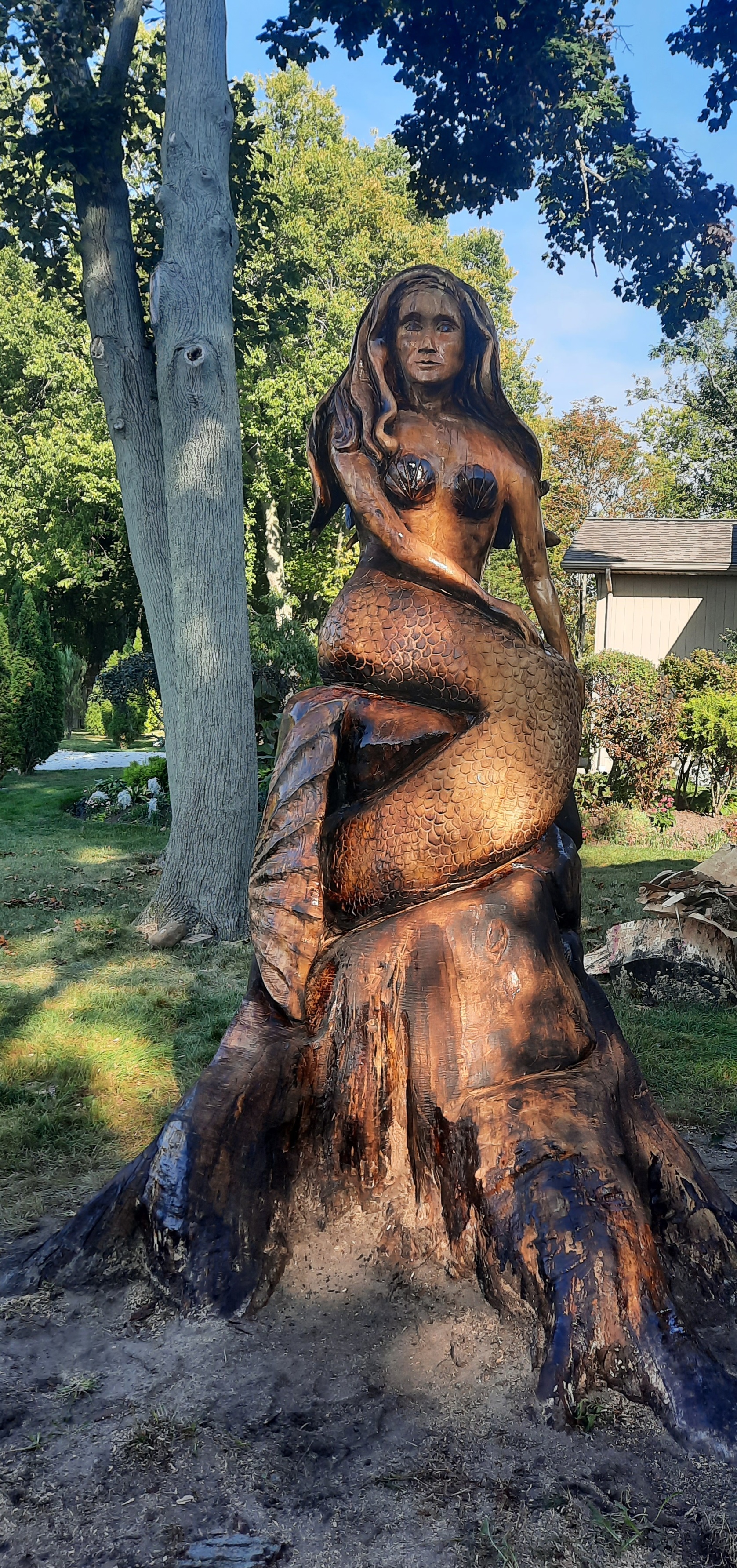 Two wood carvers using chainsaws to create large animal sculptures outside a modern home