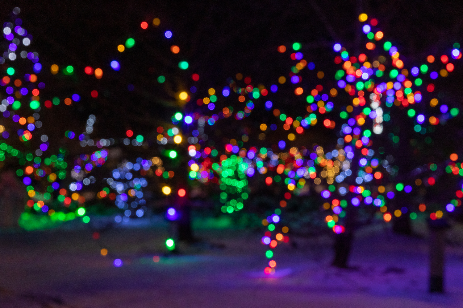 Winter festival scene with people walking through a snow-covered village adorned with string lights and wooden stalls, under a starry sky.