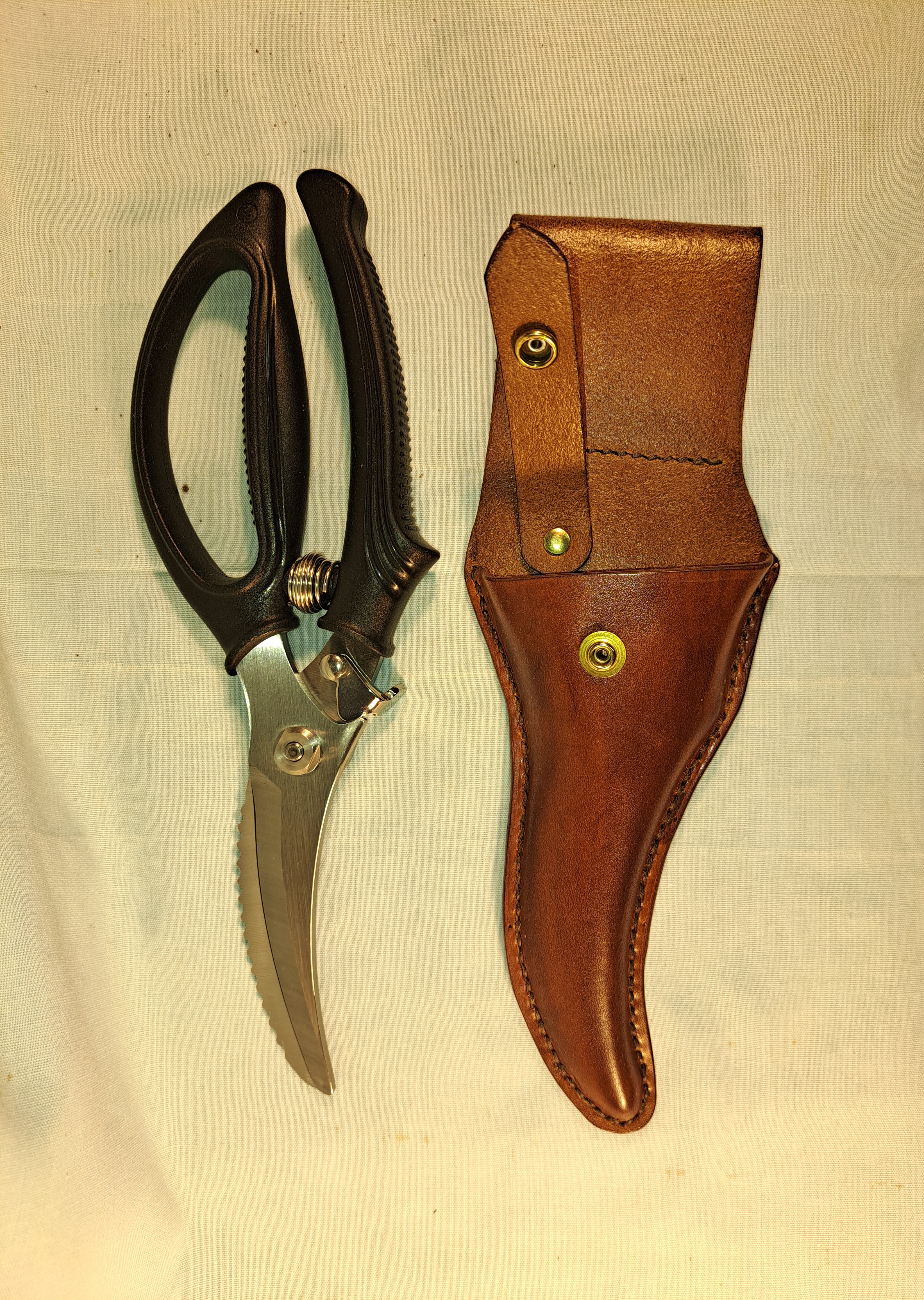 A brown custom leather sheath sitting next to a pair of scissors