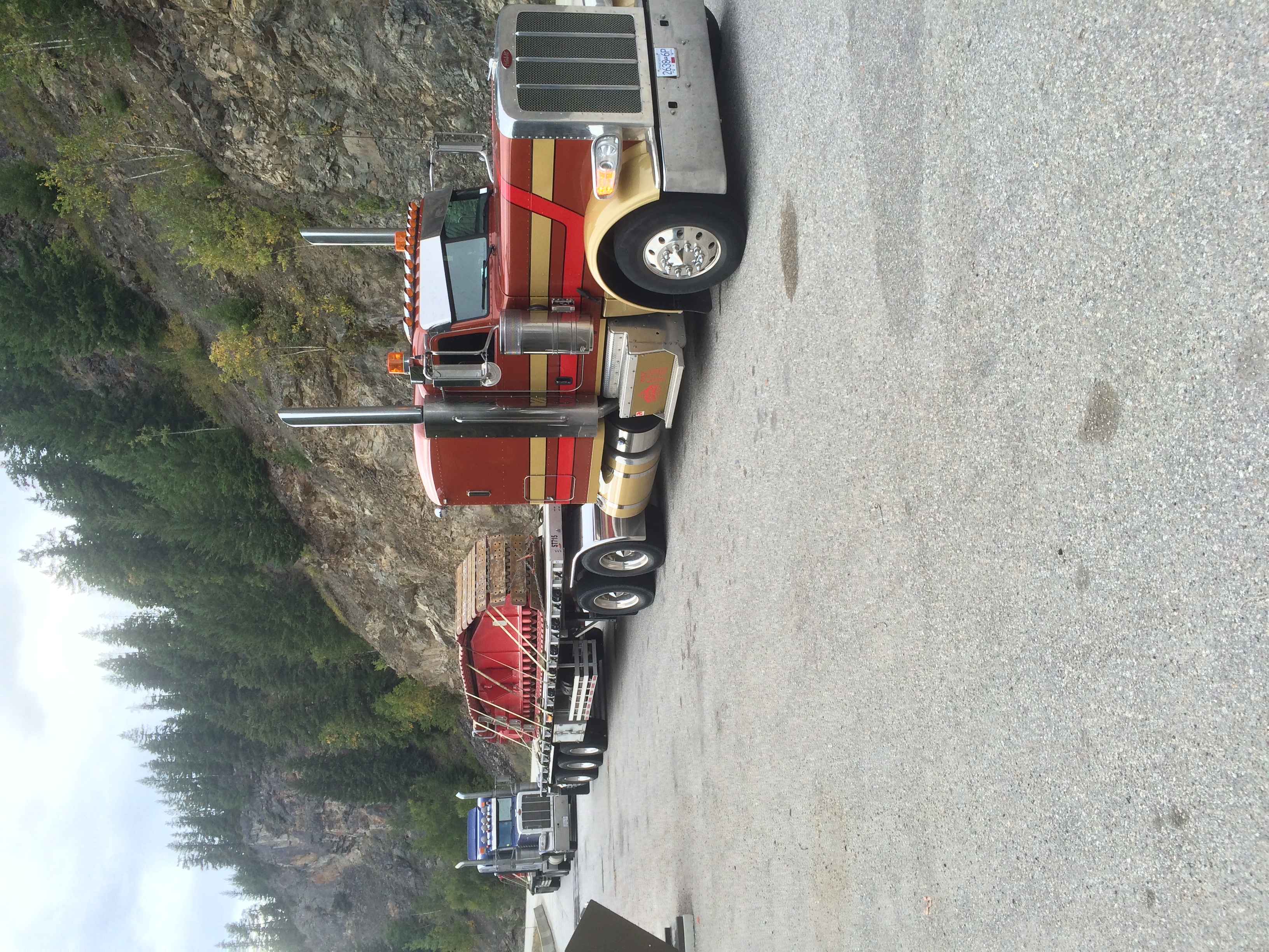 Heavy-duty truck transporting construction equipment on flatbed trailer with blue sky and trees in background.