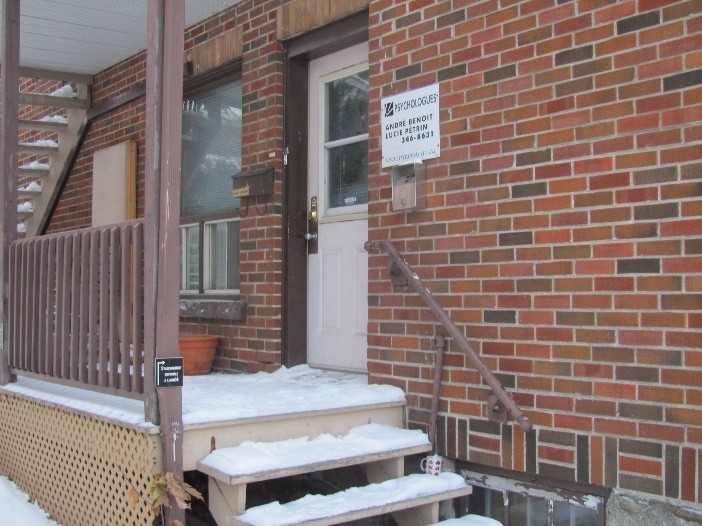 Deux femmes avec masques discutent dans un couloir d'hôpital, avec panneaux d'information en arrière-plan.