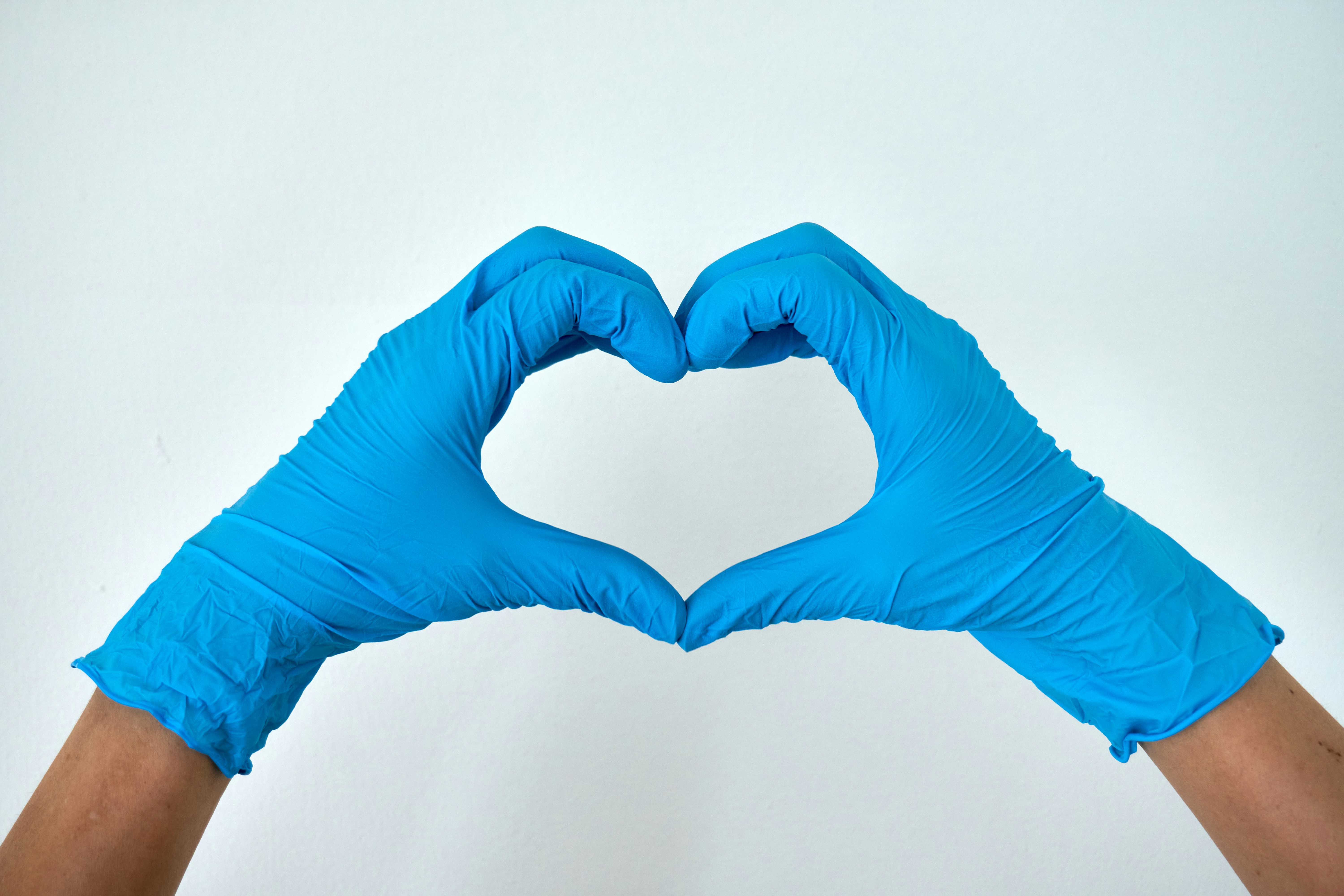 Hands wearing blue nitrile gloves forming a heart shape on a light background