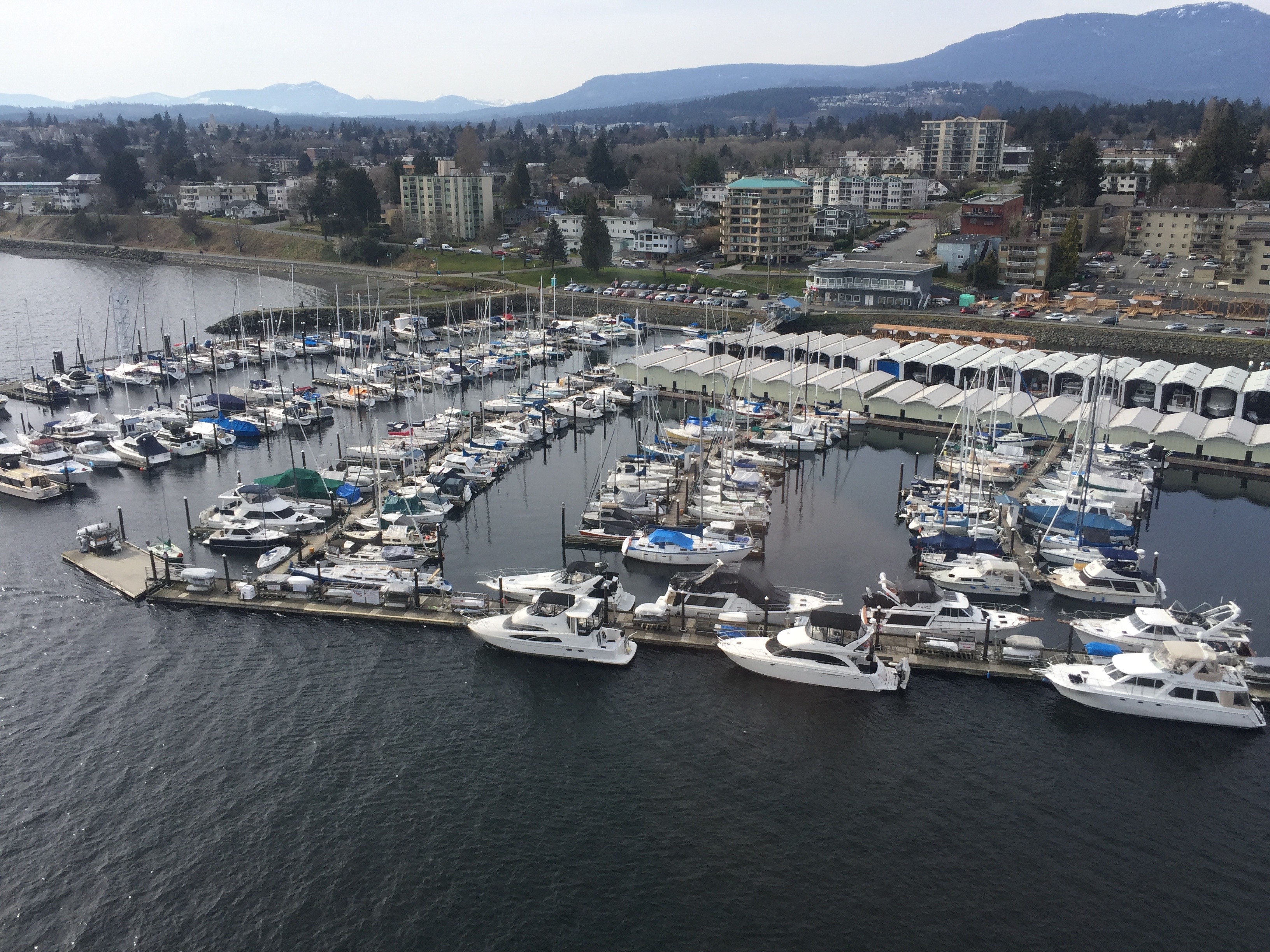 Aerial view of a marina with numerous docked boats, surrounded by urban buildings and proximity to mountainous landscape.