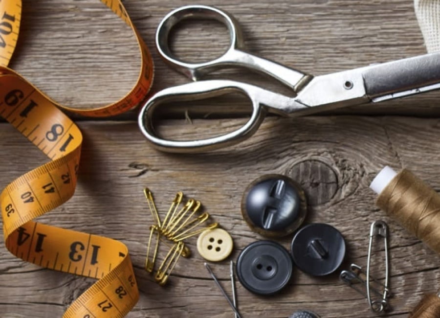 Sewing tools and materials on a wooden surface, including scissors, measuring tape, buttons, thread, and safety pins.
Sewing tools and materials on a wooden surface, including scissors, measuring tape, buttons, thread, and safety pins.