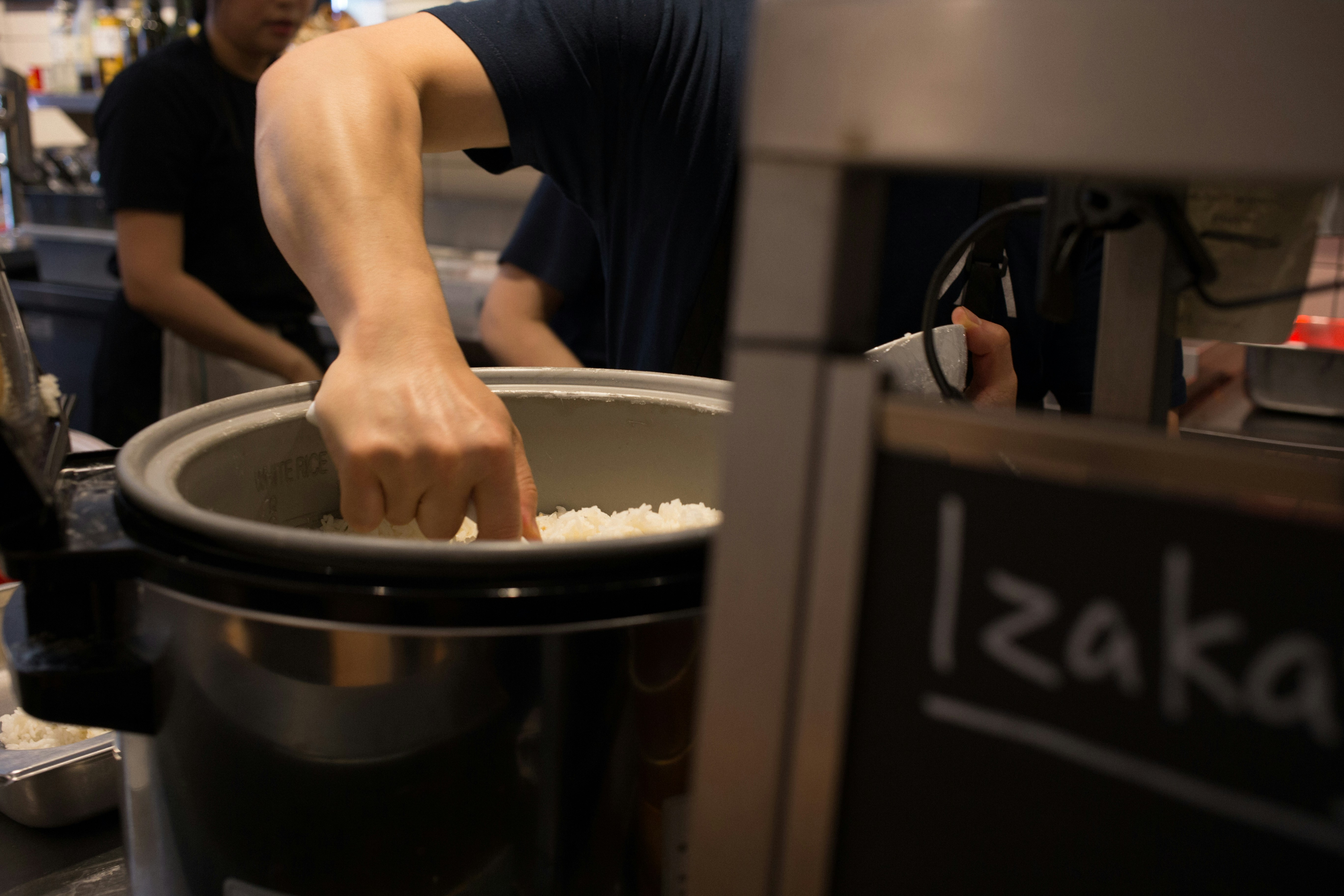 Person scooping rice from a large rice cooker in a kitchen setting. Person scooping rice from a large rice cooker in a kitchen setting.