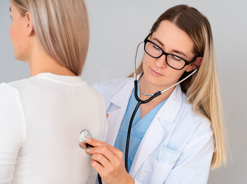 Female doctor using stethoscope to examine a patient's back during medical checkup