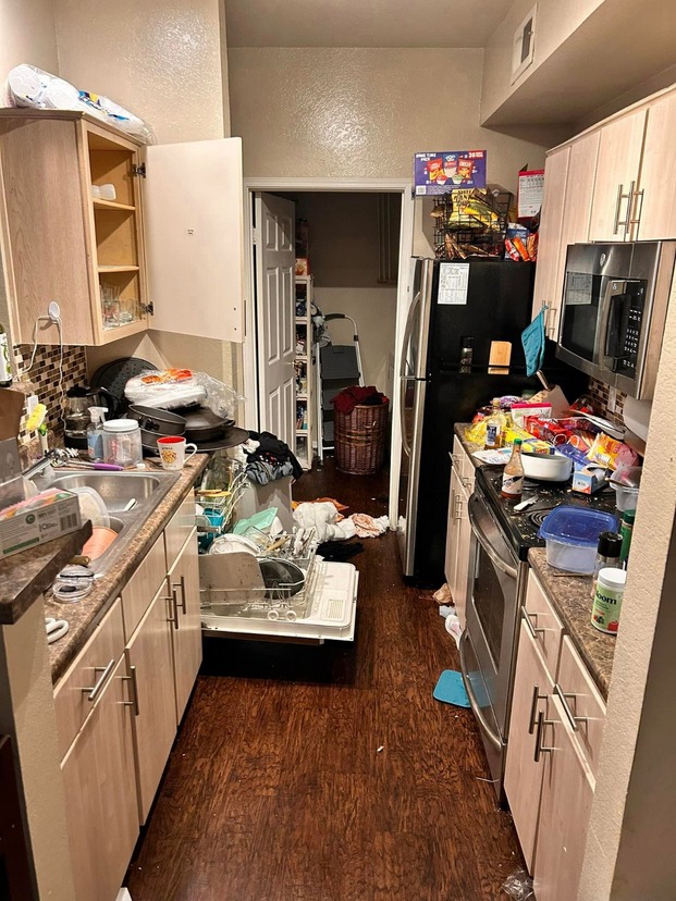 Kitchen in neglected property condition with clutter accumulation, disrupted surfaces, and environmental overwhelm requiring structured restoration