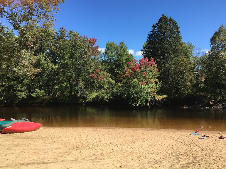 Paysage de montagne avec rivière, chalets, tente, et personnes sur des bouées.